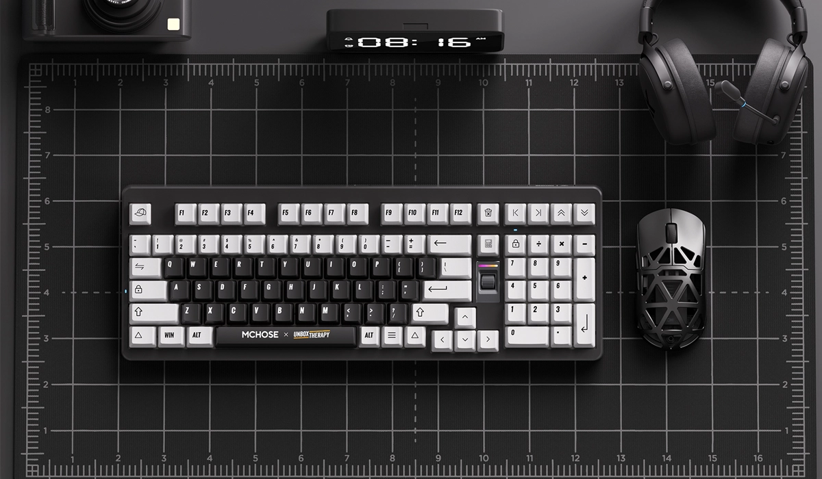 Na czarnym biurku leży klawiatura MCHOSE z białymi i czarnymi klawiszami, obok myszka i słuchawki.
